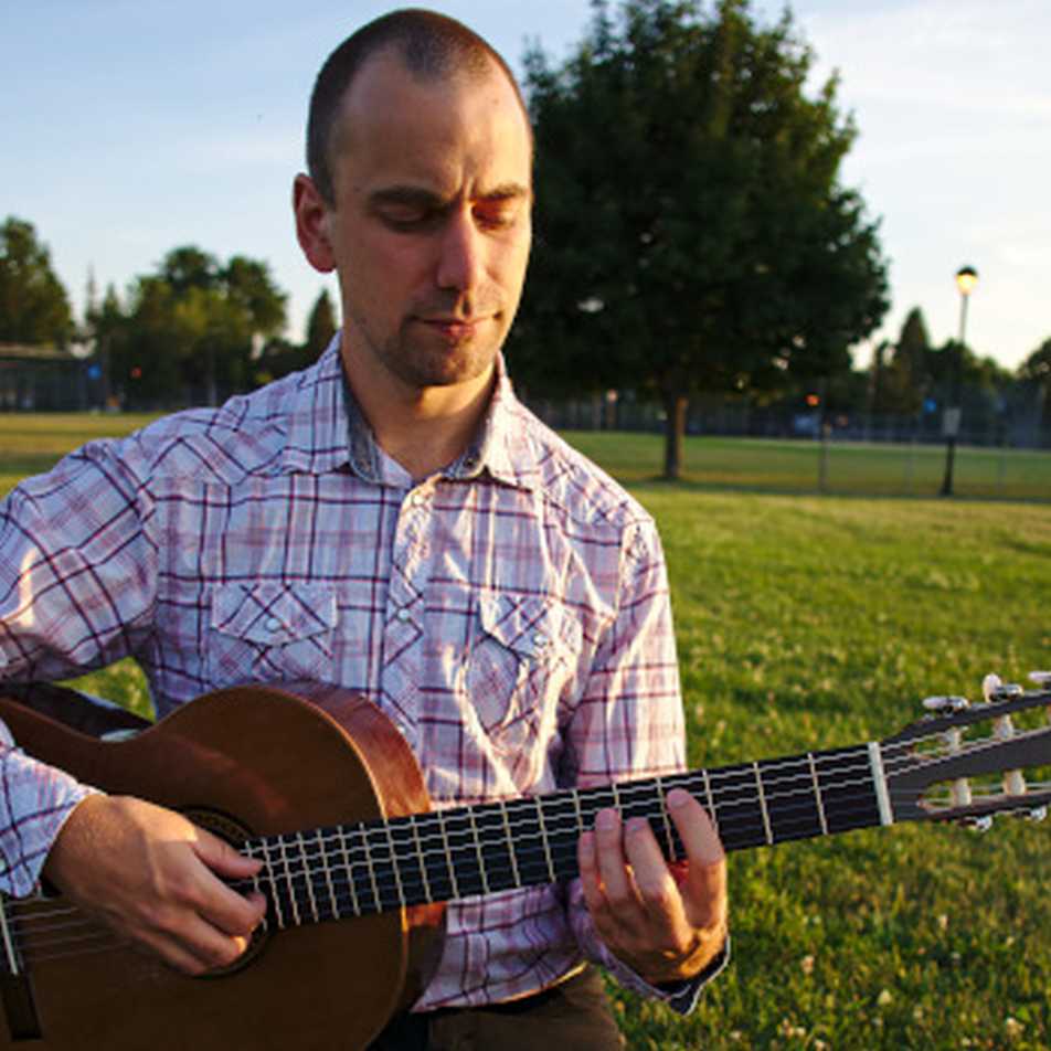 Expert guitarist Brett Vachon playing a classical guitar in the park
